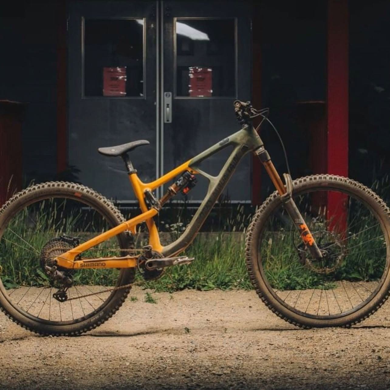Custom-painted orange and olive enduro bike parked in front of a dark building